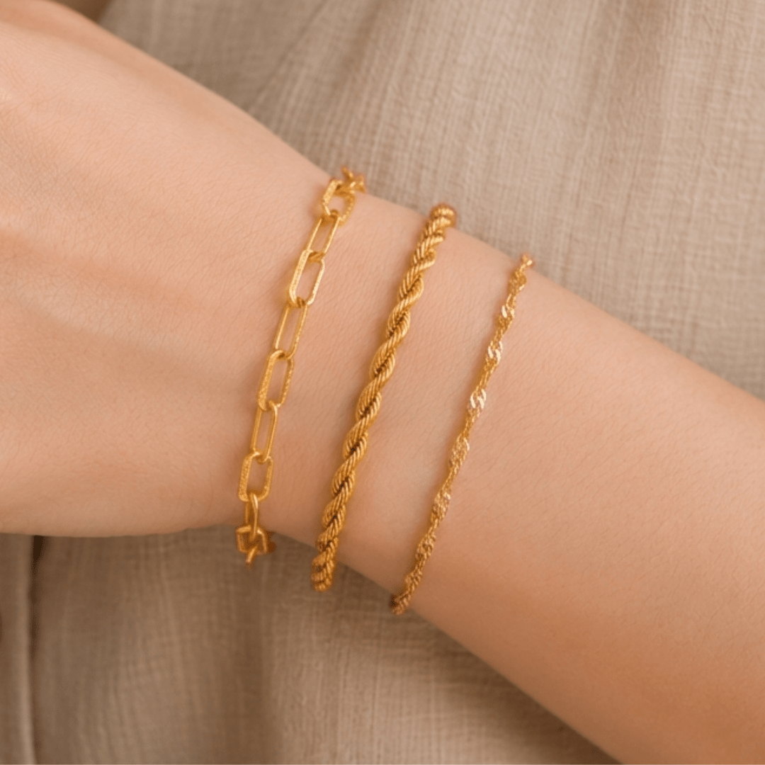 Three gold bracelets on a wrist against a neutral background