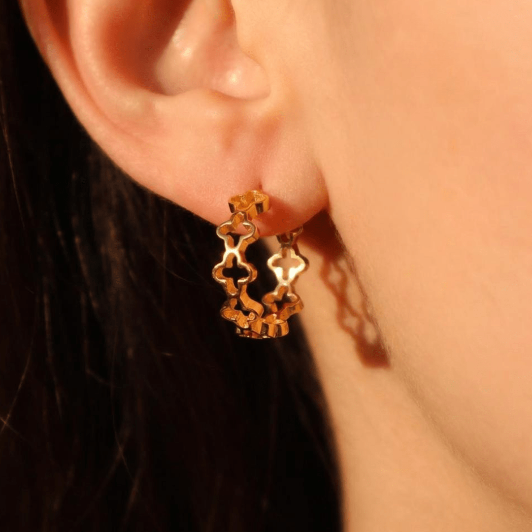 Gold earrings worn by a woman against a blurred background