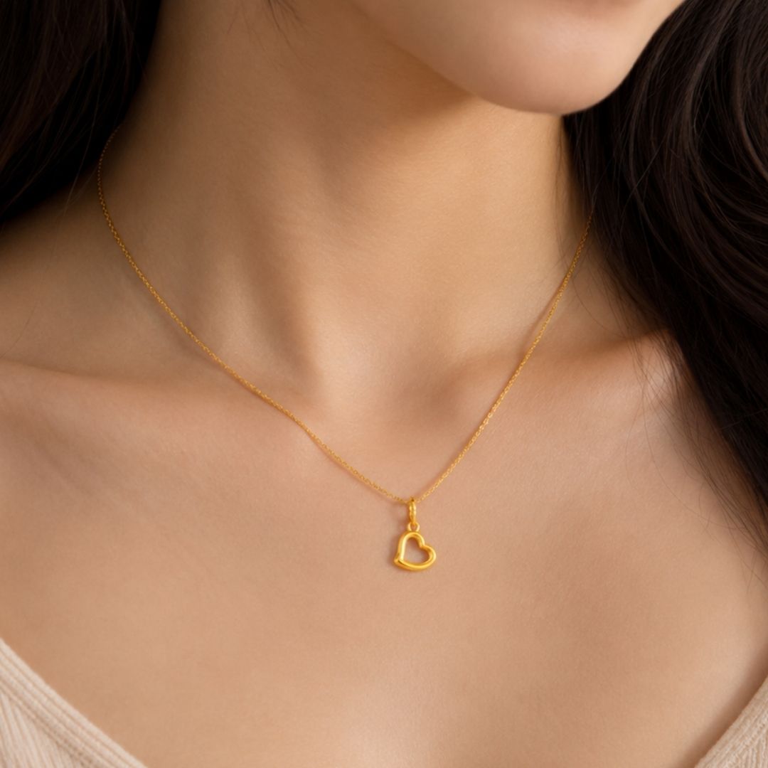 A close-up of a model's neck and chest wearing a delicate gold chain necklace with a small open heart pendant.